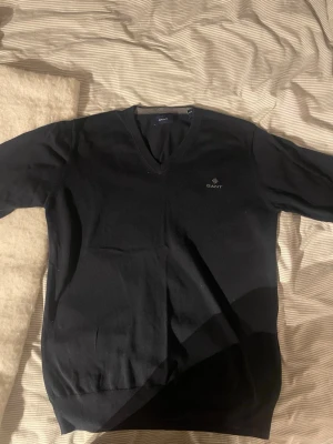 Mörkblå V-ringad tröja från GANT - Klassisk svart V-ringad tröja från GANT med diskret logga på bröstet. Tillverkad i mjukt material som sitter snyggt på kroppen. Perfekt att bära över en skjorta eller t-shirt för en clean och stilren look. Nypris ligger på typ 1400kr, mitt pris: 500kr. Denna är i storlek s men passar även storlek m. 