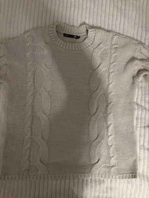 Beige kabelstickad tröja - Snygg beige kabelstickad tröja från lager 157 med rund halsringning och fina mönster längs fram- och baksidan. Tröjan har ribbade muddar vid hals, ärmslut och nederkant. Perfekt för lager på lager och enkel att matcha.
