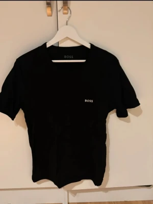 Svart t-shirt från BOSS - Snygg svart t-shirt från BOSS med diskret logga på bröstet. Klassisk rund halsringning och korta ärmar. Tillverkad i mjuk bomull som känns skön mot huden. Perfekt basplagg för en clean och stilren look.Priser kan diskutera!
