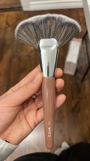 CAIA F02 sminkborste - Snygg och stor solfjäderformad sminkborste från CAIA, modell F02. Handtaget är glansigt beige-brunt och borsten har täta, mjuka strån i svart, vitt och grått. Perfekt för highlighter eller att svepa bort överskottspuder. Metallfäste i silver ger en lyxig känsla.
