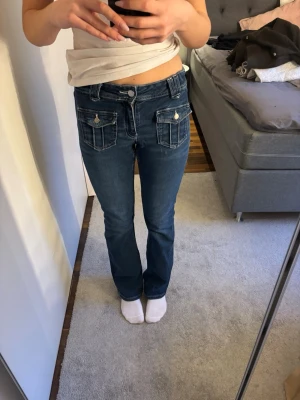 Blå bootcut jeans med fickor fram - Säljer ett par blå bootcut jeans med två fickor framtill med  knappar. Jeansen har normal midja och klassiska bakfickor.  Sköna att bära, perfekta till vardagslooken. Materialet är denim i bomull.