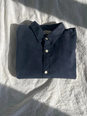 Mörkblå bomullsskjorta med knappar - Stilren mörkblå skjorta i bomull med klassisk krage och vita knappar framtill. 