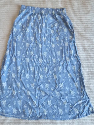 Blommig blå långkjol - Söt blå långkjol från lager 157  med vitt blommigt mönster. Kjolen har resår i midjan för en bekväm passform och är gjord i ett lätt och mjukt material, perfekt för varmare dagar. Enkel att styla med både sneakers och sandaler.