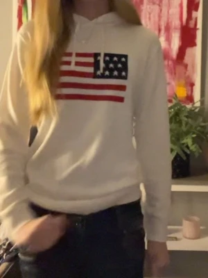 Vit hoodie med amerikansk flagga - Vit hoodie med tryck av amerikanska flaggan på bröstet. Perfekt för en avslappnad och cool stil.
