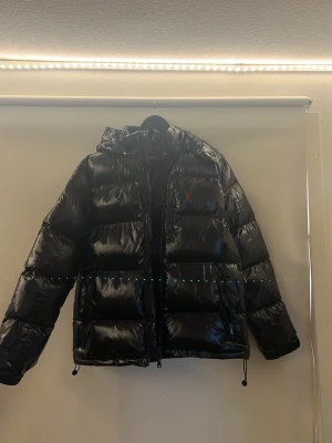 Svart glansig jacka från polo RalphLauren XS - Riktigt snygg och bekväm vinterjacka ifrån polo ralphlauren, storleken är XS i vuxen storlek och den passar dig som är 175-182cm  skulle jag säga, jag är ungefär 180cm och på sista bilden kan ni se hur den sitter.  säljes nu eftersom jag inte har användning av den längre, jackan har använts ungefär kanske 2 gånger (kan hitta lappen som satt om det önskas men kan ta lite extra tid isåfall) den är som sagt väldigt bekväm och varm också, inget man fryser med i minus grader direkt.Kom pm för frågor😁