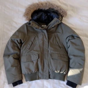 Grön/militärgrön y2k jacka/vinterjacka/bomberjacka, storlek 34 - Militärgrön vinterjacka från Everest i bra kvalitet. I fint använt skick. Yttertyg och foder 100% nylon, fyllning 50% dun och 50% fjäder. Snygg och varm med avtagbar fuskpäls och flera bra fickor. 