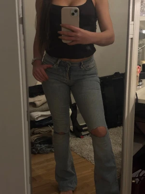 Bootcut jeans  - Säljer ett par ljusblå bootcut jeans med hål på båda knäna. Jeansen har klassisk femficksdesign och är i ett mjukt denimtyg. Perfekta för en avslappnad och trendig look.