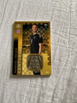 Match Attax Centurion kort Bayern München - Samlarobjekt: Match Attax Centurion kort från Topps med motiv av FC Bayern München och guld/svart design. Kortet har Champions League-tema och klubbens logga samt en medaljliknande detalj på framsidan. Perfekt för fotbollsentusiaster och samlare. Värd 520 kr
