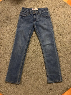Levi's 501 blå jeans 140 cm - Klassiska blå Levi's 501 jeans med rak passform och femficksmodell. Tillverkade i bomull med snygga kontrastsömmar och ikonisk bakficka. Perfekta för dig som gillar tidlös denimstil.