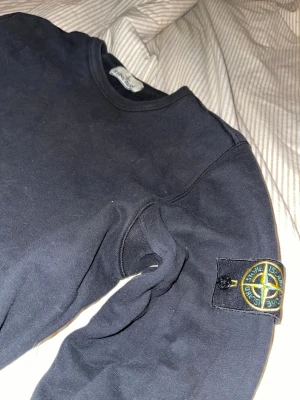 Svart tröja från Stone Island - Säljer en svart sweatshirt från Stone Island med den klassiska logotypen på ärmen.  Den är inte använd på flera år nu då jag vuxit ur den sedan länge så den är i princip nyskick! Jag köpte den på Johnells online 2019 så givetvis äkta med digitalt kvitto kvar. QR kan fås i pm. True to size