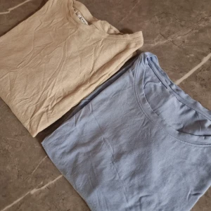Beige och ljusblå t-shirt Holly & Whyte - Två t-shirts ena är från Holly & Whyte by Lindex i storlek XL. Den ena är beige och den andra ljusblå, båda med klassisk rund hals och korta ärmar. Perfekta för en chill och avslappnad look, tillverkade i mjuk bomull.