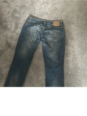 Blå jeans med detaljerade bakfickor - Säljer ett par blå jeans med snyggt slitna detaljer och kontrastsömmar. Bakfickorna har dekorativa sömmar och en liten metall-detalj. Jeansen har en klassisk femficksmodell och är tillverkade i denim.