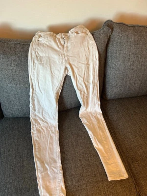 Vita skinny jeans med mid midja - Säljer ett par vita skinny jeans med mid midja och klassisk femficksdesign. Jeansen har smal passform och dragkedja med knapp framtill. Perfekta för dig som vill ha en clean och stilren look.