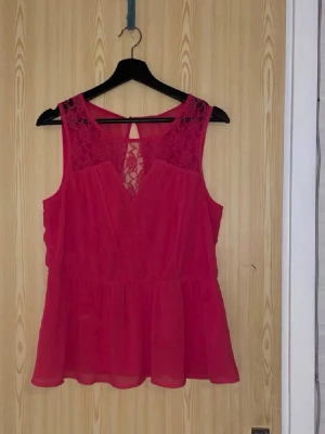 Rosa ärmlös topp med spetsdetaljer - Säljer en snygg rosa ärmlös topp med spetsdetaljer både fram och bak. Toppen har en lätt utsvängd passform och ett transparent lager över axlarna. Perfekt för dig som gillar feminina detaljer och vill sticka ut lite extra.