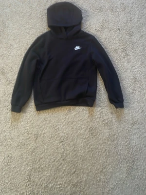 Svart hoodie från Nike med logga - Snygg svart hoodie från Nike med klassisk broderad vit logga på bröstet. Hoodien har huva och en stor magficka framtill. Tillverkad i mjukt material som passar perfekt för en avslappnad stil. Pris går att diskutera
