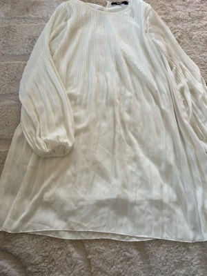 Vit plisserad klänning från BikBok - Säljer en vit plisserad klänning från BikBok i storlek M. Klänningen har långärmade ballongärmar med resår vid ärmslut och en lös, flowy passform. Materialet känns lätt och luftigt, perfekt för varmare dagar.