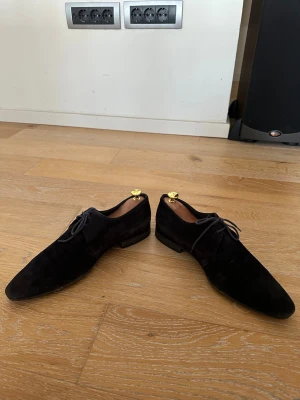 Svarta mocka loafers med snörning - Säljer ett par stilrena svarta loafers i mocka med klassisk snörning och låg klack. Skorna har en elegant, smal siluett och är perfekta för dig som gillar en clean och tidlös look. Passar till både jeans och kostymbyxor. De är använda, och en liten skada vid insidan av vänster sula (se bild)