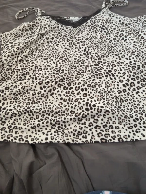 Leopardmönstrat nattlinne Primark - Säljer ett leopardmönstrat nattlinne från Primark med tunna axelband och svart spetsdetalj vid urringningen. Materialet är mjukt och lätt, perfekt för att chilla hemma. Färgen är vit med svarta och beige fläckar.