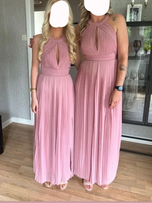 Lång plisserad rosa klänning - JAG HAR DEN I STORLEK 32 OCH 36!! Säljer en elegant långklänning i ljusrosa med plisserat tyg och hög hals. Klänningen har ärmlös design och en snygg detalj med öppning framtill. Perfekt för speciella tillfällen och har dragkedja i ryggen.