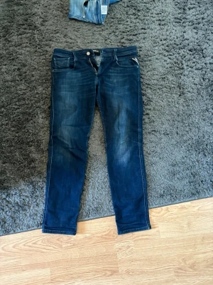 Mörkblå jeans från Replay - Säljer ett par mörkblå jeans från Replay med klassisk femficksmodell och raka ben. Jeansen har snygga slitningar framtill och kontrastsömmar. Tillverkade i denim med en skön passform och läderpatch bak i midjan.