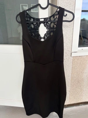 Svart klänning med spetsdetaljer - Jätte fin klänning, säljer då den aldrig kommit till användning. Helt ny. Svart klänning i figurnära modell med v-ringning och dekorativa spetsdetaljer i ryggen. Klänningen är ärmlös och har en elegant, stilren look som passar perfekt till olika tillfällen. Materialet känns mjukt och följsamt mot kroppen.