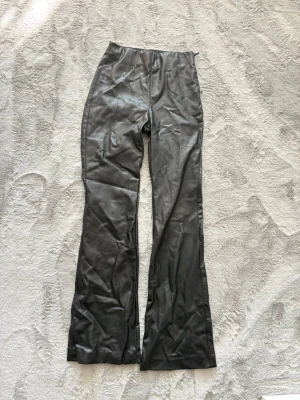 Svarta skinnbyxor med dragkedja - Säljer dessa svarta skinnbyxor med utsvängda ben och diskret dragkedja i sidan. 