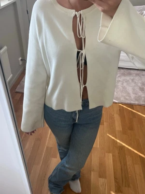 Vit cardigan med knytband - Trendig vit cardigan med vida ärmar och knytband framtill. Öppen modell som ger en avslappnad och cool look. Perfekt att styla över ett linne eller topp för en modern vibe.