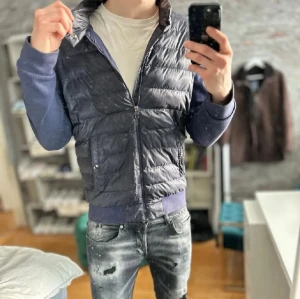 Mörkblå cardigan från Ralph lauren - Snygg mörkblå dunväst från Diesel med quiltad design och matchande blå muddar. Västen har dragkedja framtill, två fickor med tryckknappar och avtagbara ärmar i sweatshirtmaterial. Perfekt för lager-på-lager och streetwear-stil.
