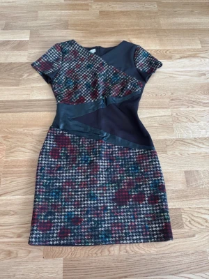 Klänning storlek S - Kortklänning med ett färgglatt rutigt mönster och svarta läderdetaljer. Från Rinascimento i storlek S.