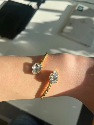 Mini Drop Bracelet Crystal armband - Snyggt armband i tvinnad design och två stora droppformade kristaller i båda ändar. Perfekt för dig som vill ha ett statement-smycke med glittrande detaljer. Enkel att matcha med andra accessoarer.