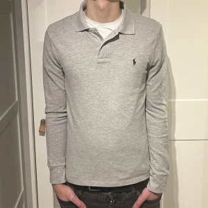 Ralph Lauren pikétröja  - Långärmad Ralph Lauren piké i färgen grå. Inga defekter på tröjan. Size S (slim fit) modellen är 176cm. Hör av dig vid funderingar!
