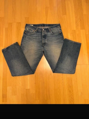 Levi's raka blå jeans (Real)  - Klassiska blå Levi's jeans med rak passform. Jeansen har en snygg tvätt med ljusare partier framtill och bak, samt en läderpatch bak i midjan. Tillverkade i slitstark denim, perfekta för en avslappnad och tidlös stil. Köpts på Levis affär (Real) 