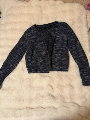 Mörkblå zip-kofta från Gina Tricot - Mysig mörkblåmelerad kofta från Gina Tricot med dragkedja framtill. Koftan har lång ärm och en kortare, rak passform. Materialet är stickat och mjukt, perfekt för lager på lager. Enkel och stilren design som passar till det mesta.