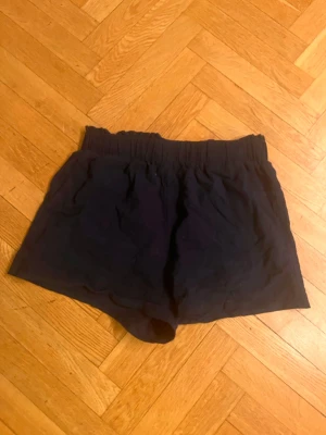 Svarta/mörkblåa höga shorts med resårmidja - Säljer ett par svarta shorts med hög midja och bred resår i midjan. Shortsen har en loose passform och är tillverkade i ett mjukt bomullstyg, perfekta för varma dagar. Inga synliga detaljer eller mönster.Skriv gärna för mått! 💕
