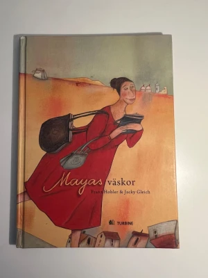 Mayas väskor - Franz Hohler - En fantasifull skönlitterär bok med hårda pärmar, illustrerad framsida i varma färger och titeln 'Mayas väskor'. Boken är skriven av Franz Hohler och Jacky Gleich och handlar om Maya som hamnar i en magisk värld genom sin handväska.