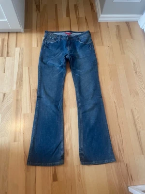 Blå lågmidjade bootcut jeans med strassdetaljer - Snygga blå lågmidjade bootcut jeans med strassdetaljer på fickorna. De är i storlek 36/10(se sista bilden) från märket Love and Peace. Innerbenslängd: 81 cm, Midjemått: 36-37 cm platt från sida till sida. Skriv om ni har några frågor💕
