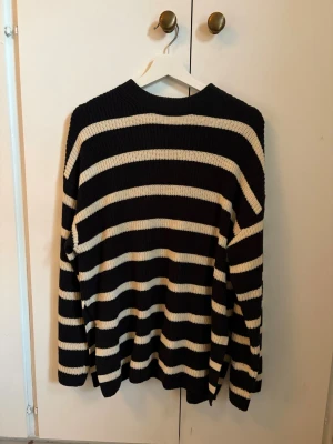 Svartvit randig stickad tröja - Säljer en oversized stickad tröja med breda svarta och vita horisontella ränder. Tröjan har rund halsringning, långa ärmar och slitsar längst ned på vardera sida. 