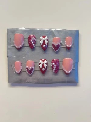 Press On Nails || Valentine Date || Size S - Söta korta almond lös naglar hand gjorda av mig. Röd och nude bas som färger tillsammans med 3d detaljer av pärlor och rosetter ❤️ Det du får med dig : * Fil och manikyr pinne * nagellim klistermärken * 2 lappar av rengöring för naglar.