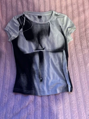 Grafisk t-shirt med kroppstryck - Cool t-shirt med grafiskt svartvitt tryck som föreställer en kropp. T-shirten har rund hals, korta ärmar och är figurnära i modellen. Materialet känns mjukt och stretchigt, perfekt för en edgy och unik stil.