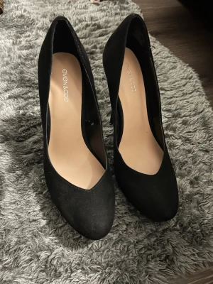 Svarta pumps från Even&Odd - Stilrena svarta pumps från Even&Odd med hög klack och platåsula. Skorna har rundad tå och är tillverkade i ett mockaliknande material som ger en snygg matt finish. Perfekta för dig som vill ha en klassisk och trendig look.