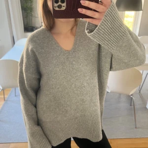 Grå oversized stickad tröja - Mysig grå stickad tröja med v-ringning och breda ribbade muddar vid ärmslut och nederkant.