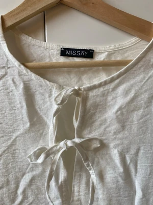 Vit långärmad klänning från Missay - Luftig vit klänning från Missay med långa ärmar och två dekorativa knytband framtill. Klänningen har en avslappnad passform och volangdetaljer nedtill, vilket ger en bohemisk känsla. Perfekt för varma dagar och enkel att styla för t.e.x. skolavslutning, student, midsommar osv!! aldrig använd