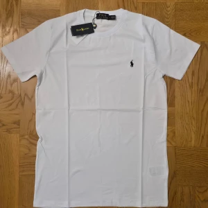 Vit t-shirt från Ralph Lauren - Klassisk vit t-shirt från Ralph Lauren med den ikoniska lilla loggan broderad på bröstet. T-shirten har rund halsringning och korta ärmar. Perfekt basplagg med normal passform och mjukt bomullsmaterial.