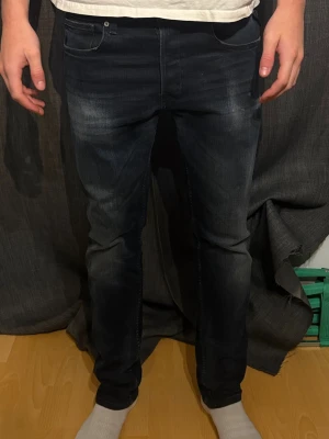 Mörkblå replay jeans  - Säljer ett par mörkblå  jeans från replay med en snygg tvätt och klassiska fem fickor. Jeansen har en straight fit och subtila slitningar framtill för en modern look. Midjemått 33 och längd 30. Använda 10 gånger max. 