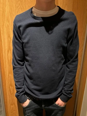 Mörkblå basic tröja i bomull från Jack &jones - En enkel och stilren mörkblå tröja med rund halsringning och långa ärmar. Tröjan är tillverkad i mjuk bomull och har ribbade muddar vid ärmslut och nederkant. Perfekt för en clean och avslappnad look.