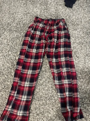 Rödrutiga pyjamasbyxor med dragsko - Mysiga pyjamasbyxor i röd, svart och vit rutigt mönster. Byxorna har resår i midjan och dragsko för skön passform. Perfekta för chillkvällar hemma. Tillverkade i mjukt tyg som känns bekvämt mot huden.