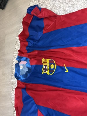 Barcelona Ronaldinho matchtröja - Säljer en klassisk Barcelona fotbollströja från Nike med Ronaldinho och nummer 10 på ryggen. Tröjan har breda röda och blå ränder, klubbmärke på bröstet och gul Nike-logga. Perfekt för dig som älskar fotboll och vill hylla en legend.