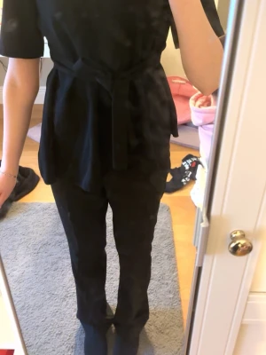 Svart topp med knyt från Zara Woman - Säljer en svart topp från Zara Woman med knyt i midjan som ger en snygg siluett. Toppen har korta ärmar och en rak passform, perfekt att styla med både jeans och kostymbyxor. Materialet känns mjukt och följsamt. Säljer pga den bara ligger i min garderob💕storlek M men passar även S.  