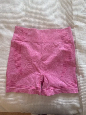 Rosa sömlösa träningstights shorts - Säljer ett par rosa sömlösa shorts perfekta för träning. De är högmidjade och har ventilerande mesh-detaljer längs sidorna och baktill för extra komfort. Materialet är stretchigt och följsamt, vilket ger en tight och bekväm passform.