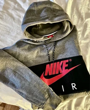 Nike Air hoodie grå svart – M streetwear unisex - Nike Air hoodie i grå/svart med röd logga. Storlek M (passar även oversize S).  Mycket fint skick – inga hål, inga fläckar. 100% äkta.                                                    Mått: Byst: ca 58 cm Längd: ca 63 cm Axelbredd: ca 66 cm Armlängd: ca 50 cm  Perfekt hoodie för streetwear/vardag.